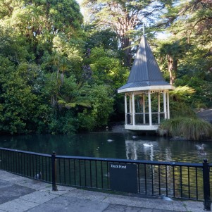 A pond with ducks and a gazebo surrounded by lush greenery.