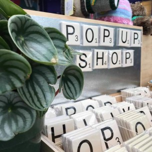 Image of the words 'Pop up shop' spelled out with square scrabble looking letter magnets with a green pot plant on the left side.